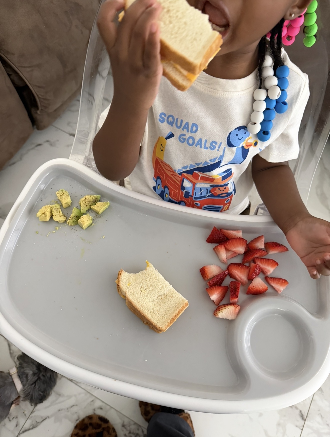 Toddler eating sandwich, avocado, and strawberries at a high chair tray - Raising children by Birth Chart 